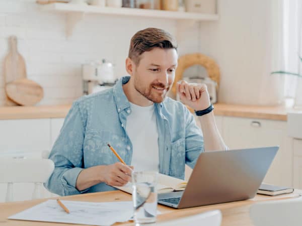 Junger Mann sitz in seiner Küche am Laptop