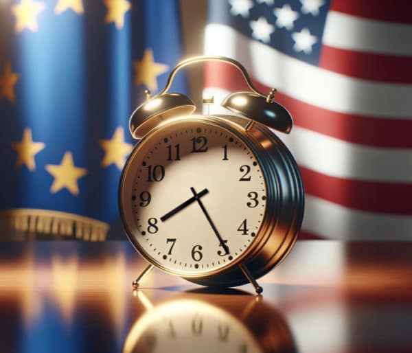 Wecker mit der Zeit 8:25 Uhr steht auf einem Tisch. Im Hintergrund die Flagge der Europäischen Union und der USA.