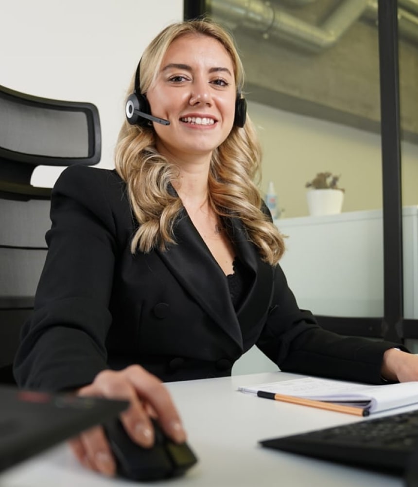 Freundliche Trading-Coachin mit Headset am Schreibtisch unterstützt Kunden beim Daytrading.
