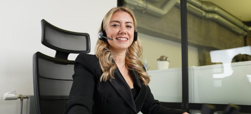 Freundliche Trading-Coachin mit Headset am Schreibtisch unterstützt Kunden beim Daytrading.